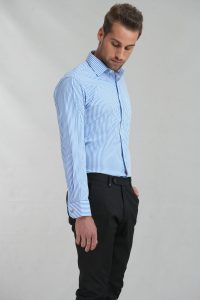 Side view of a man wearing a blue and white striped dress shirt tucked into black trousers, against a neutral backdrop.